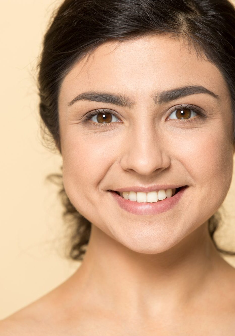 Close up head shot portrait attractive smiling indian woman looking at camera. Healthy happy hindu young lady with perfect clear skin and white toothy smile isolated on beige studio background.