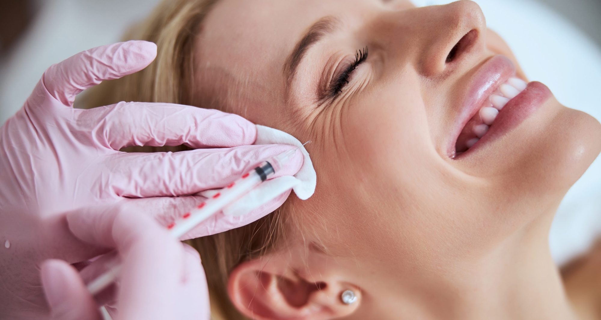 Smiling lady lying with her eyes closed during the rejuvenation injection administered by a professional dermatologist